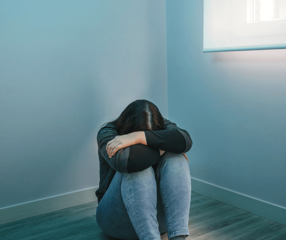 eine Frau sitzt auf dem Boden eines leeren Raumes, sie hat die Knie hochgezogen, den Kopf zwischen den Armen darauf abgelegt