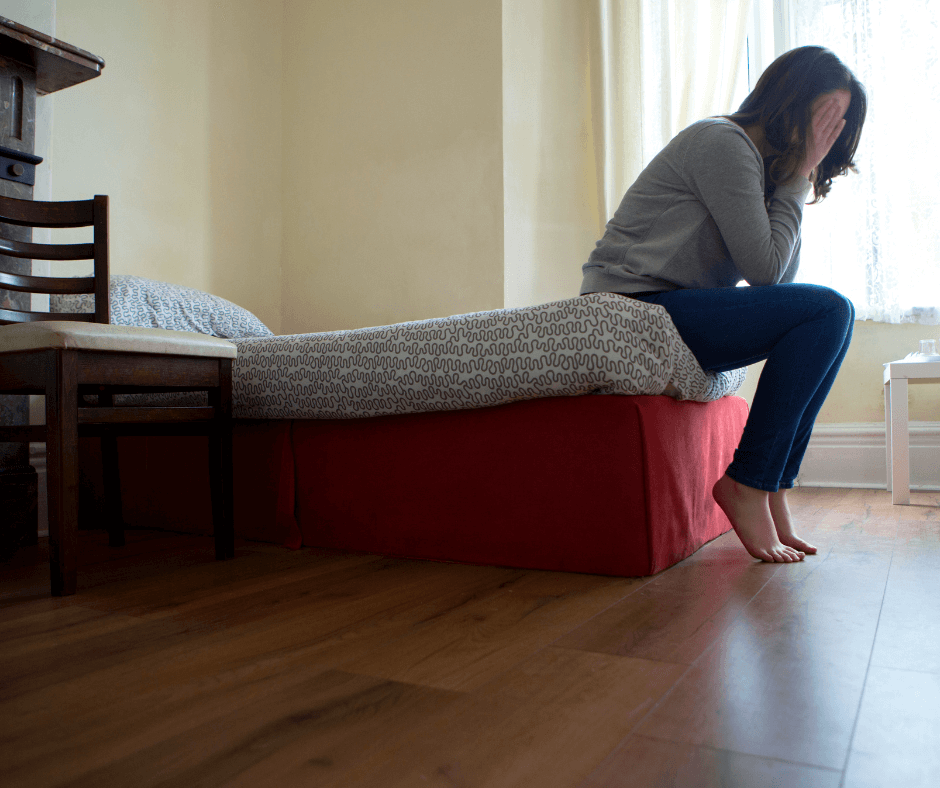 Eine Frau sitzt auf dem Bett, versteckt ihren Kopf zwischen den Händen, Scham 