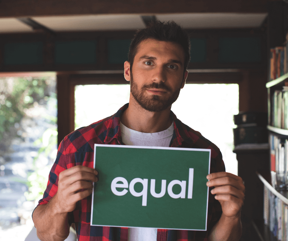 Ein Mann mit dunklen Haaren und Bart hält ein Schild hoch auf dem "equal" steht