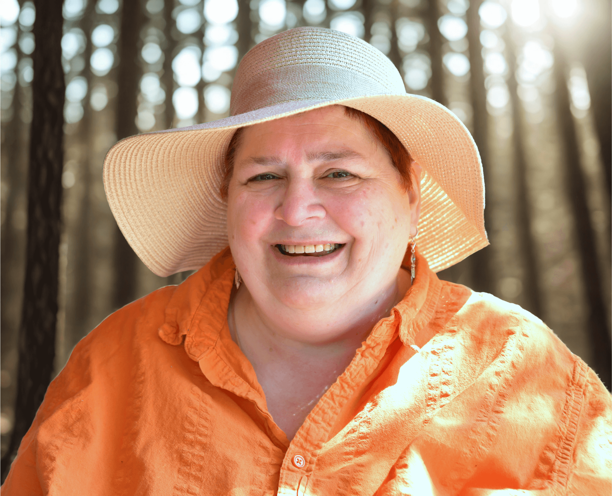 ich trage eine orange bluse und einen großen Sonnenhut vor einem Waldhintergrund