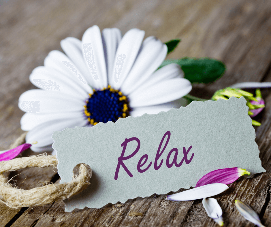 eine weiße Margeritenblüte, davor ein kleines Schildchen mit der Aufschrift Relax. Könnte auch zum Programm PAUSE, ich bin dann mal ich passen