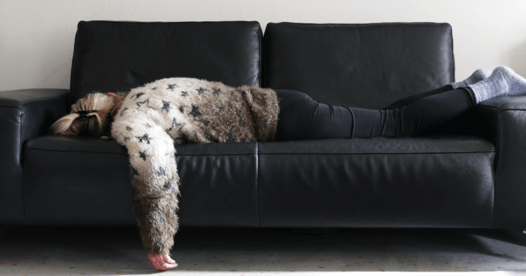 eine völlig erschöpfte Frau liegt bäuchlings auf dem Sofa